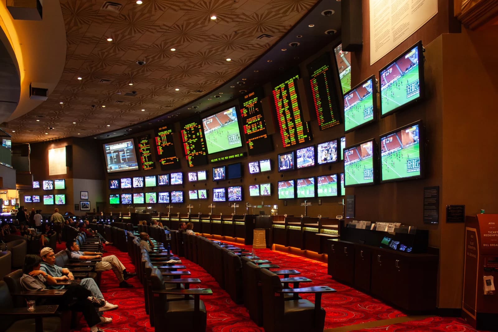 People seated in a large sportsbook room with many screens showing sports events and odds.