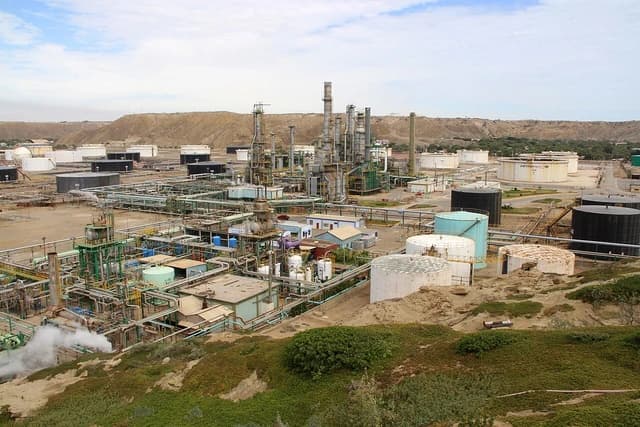 An expansive oil refinery with multiple towers, pipes, and large storage tanks under a partly cloudy sky.