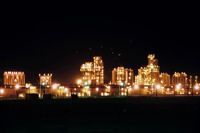 Mina Al-Ahmadi oil refinery illuminated at night with bright lights.