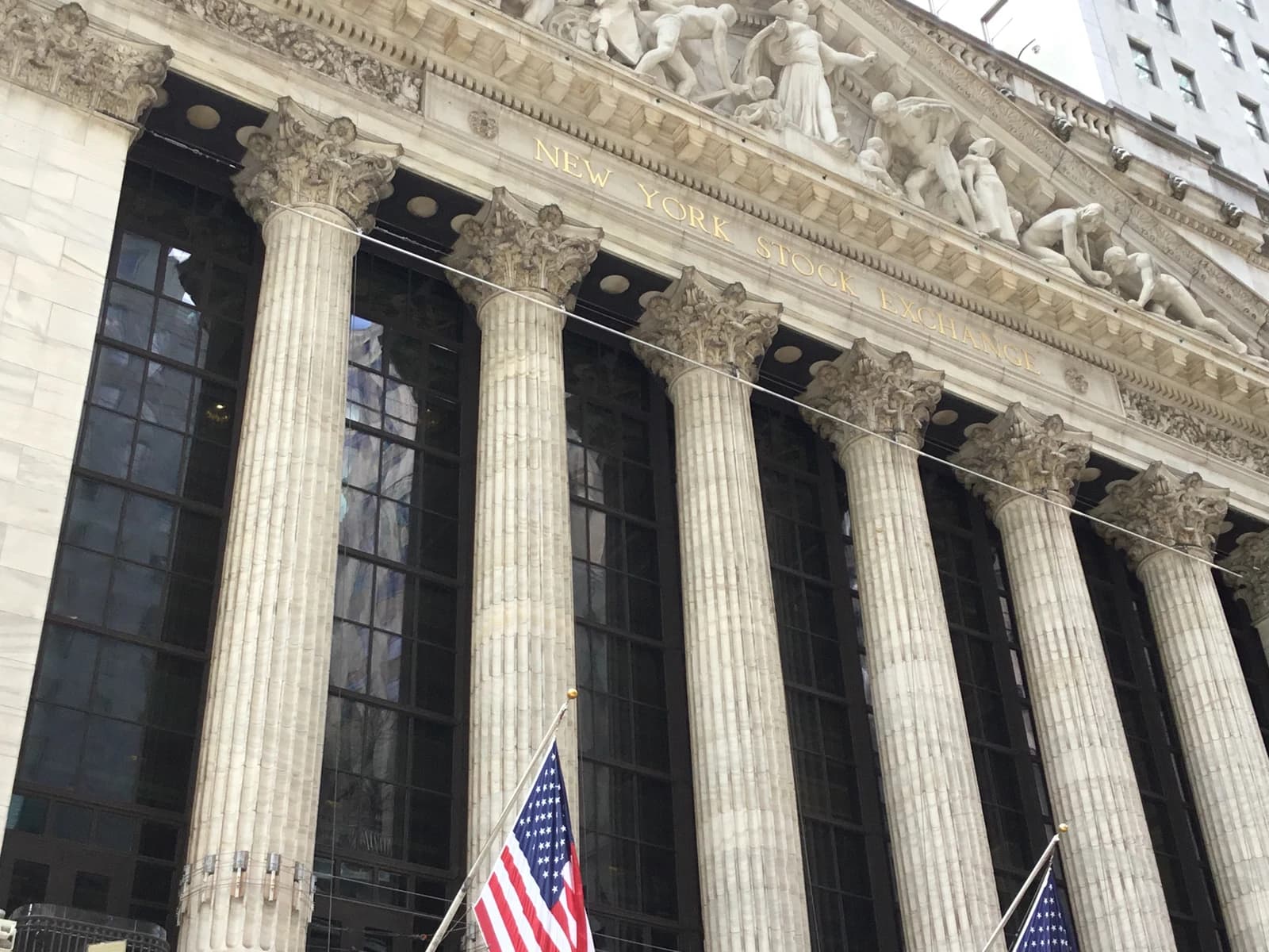 Exterior facade of the New York Stock Exchange building with pillars and American flags.