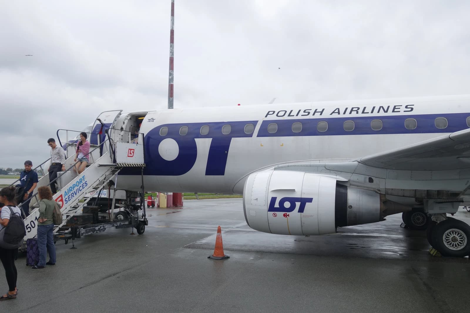 Passengers boarding a white and blue LOT Polish Airlines aircraft from a mobile staircase.