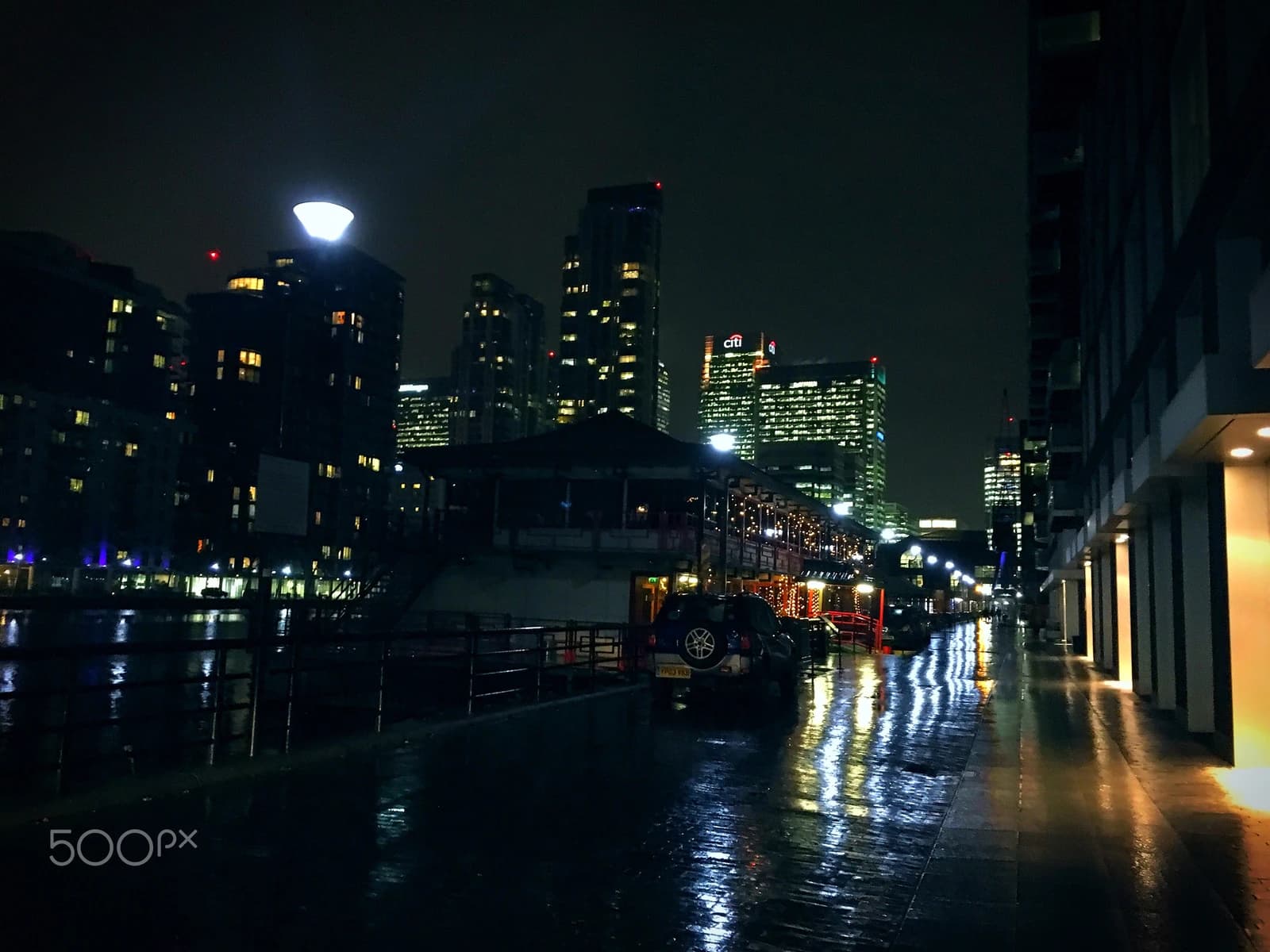 Financial skyscrapers and reflections on wet pavement in London's financial district at night.