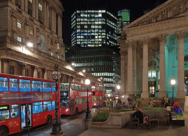 Threadneedle Street in London at night with red double-decker buses on the street.