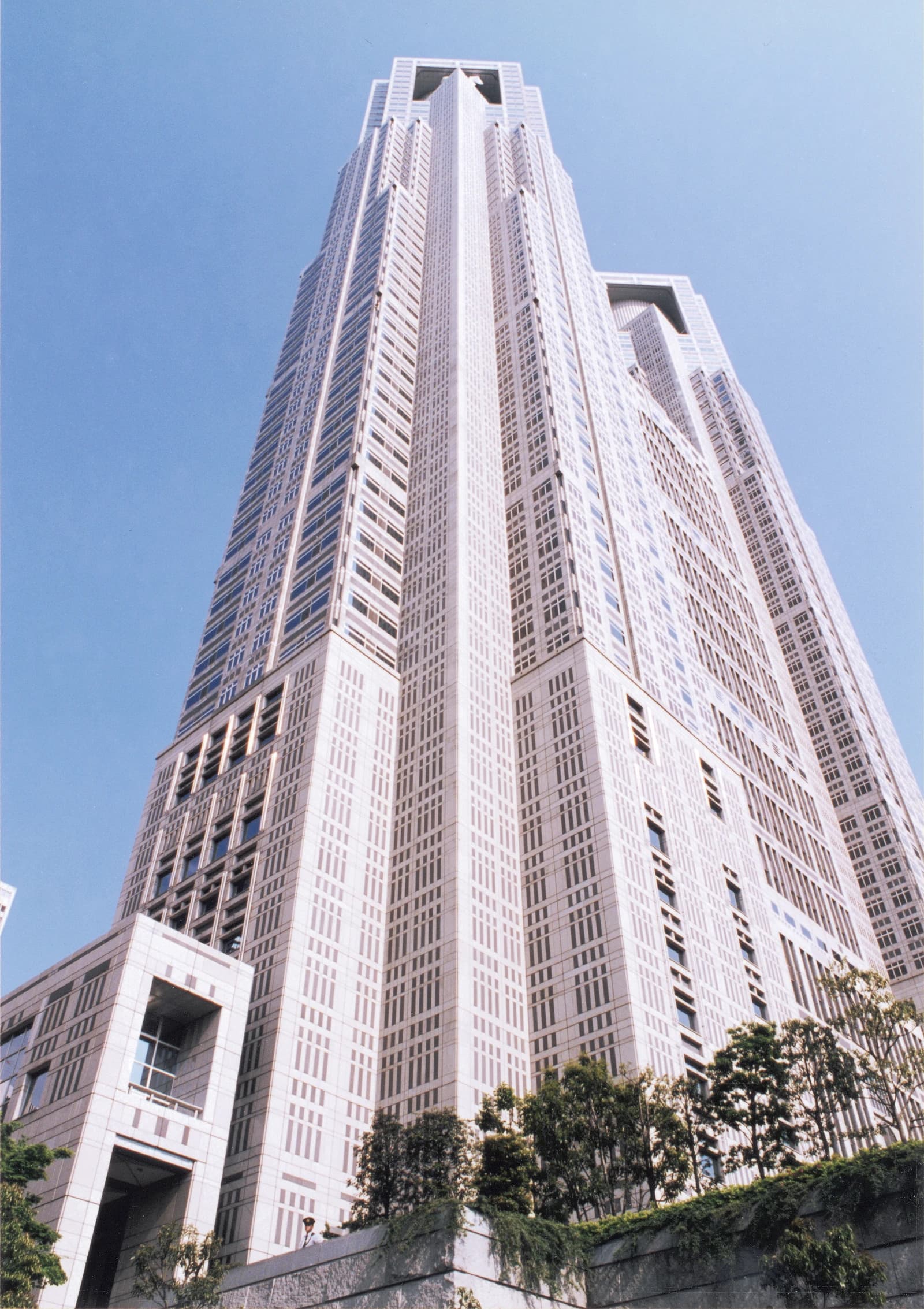 The Tokyo Metropolitan Government Building, a tall skyscraper, viewed from below against a blue sky.
