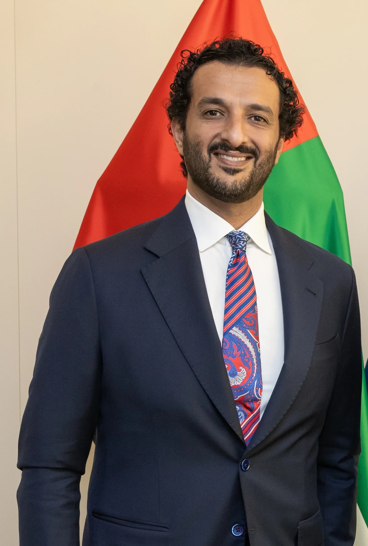 Abdullah Bin Touq Al Marri, UAE Minister for Economy, standing in front of a flag.