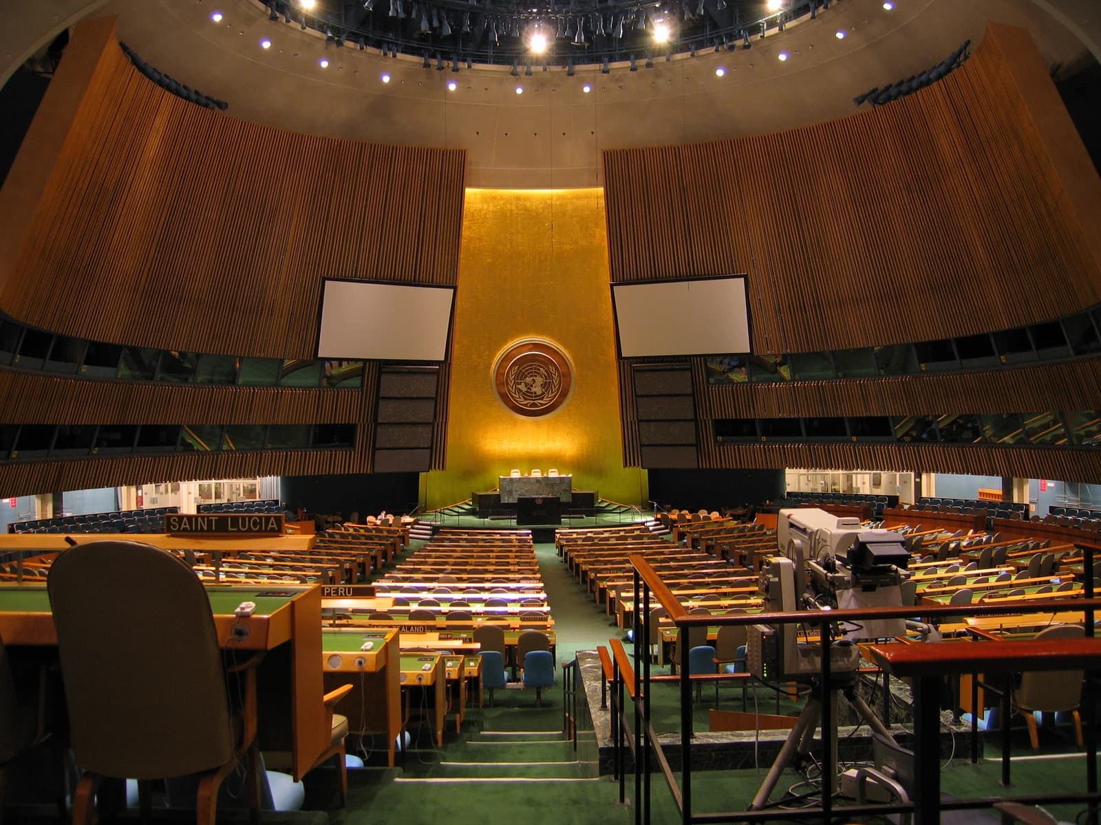 Interior of the empty United Nations General Assembly Chamber, showing delegate desks and a large emblem.