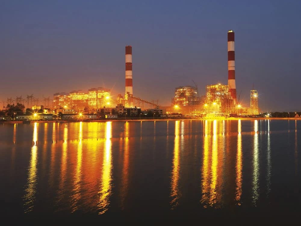 Adani Power's Tirora thermal power plant glowing at night next to a body of water.