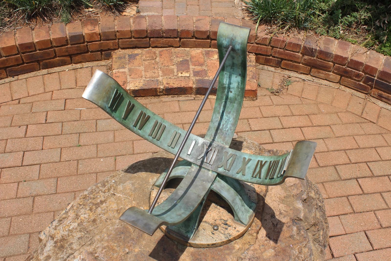 Bronze sundial with Roman numerals on a stone base at botanical garden.