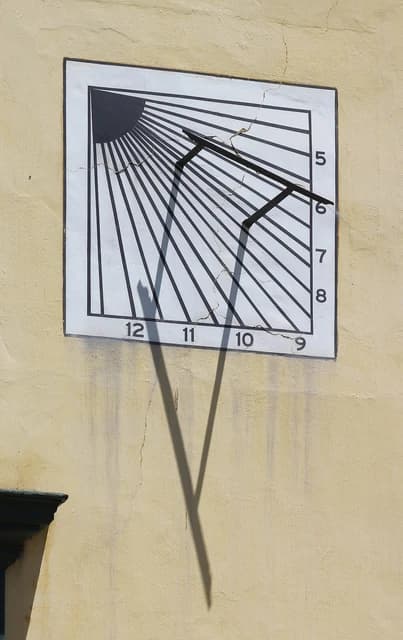 Vertical sundial showing lines and numbers for telling time, mounted on a yellow wall.
