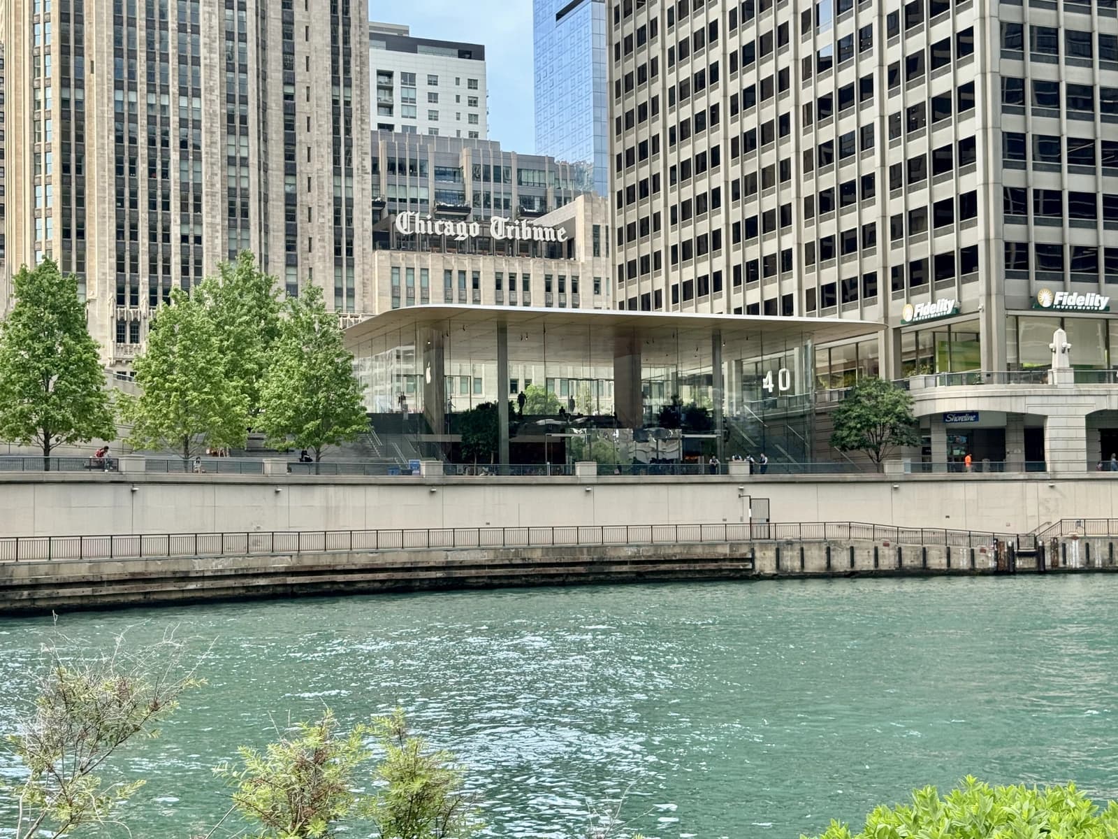 Apple Store building, glass architecture, along the Chicago River, with surrounding city buildings.