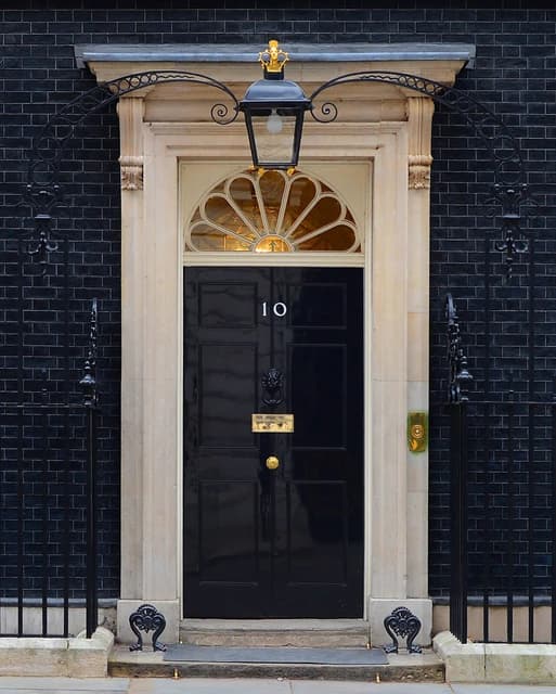 The black front door of 10 Downing Street in London, with a lamp above it.