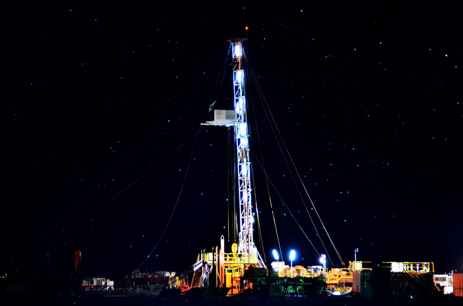 An oil drilling rig stands brightly lit against a dark, starry night sky.