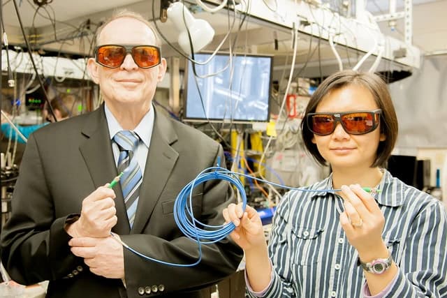 Two scientists wearing protective glasses hold optical fibers in a laboratory setting.