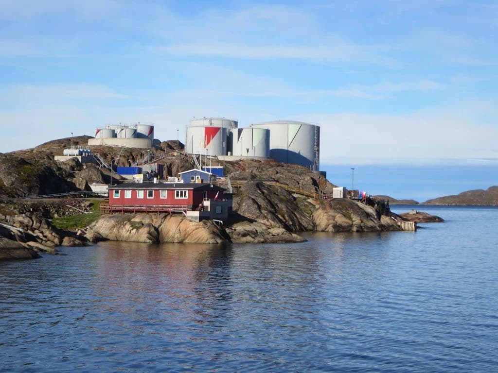 Several large oil storage tanks sit on a rocky hill overlooking a bay.