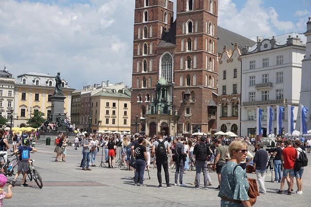 People walking around Main Square with St. Mary's Basilica and buildings in Kraków, Poland.