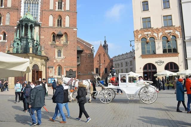 People walk and horse-drawn carriages move through the Old Town Market Square in Kraków, Poland.