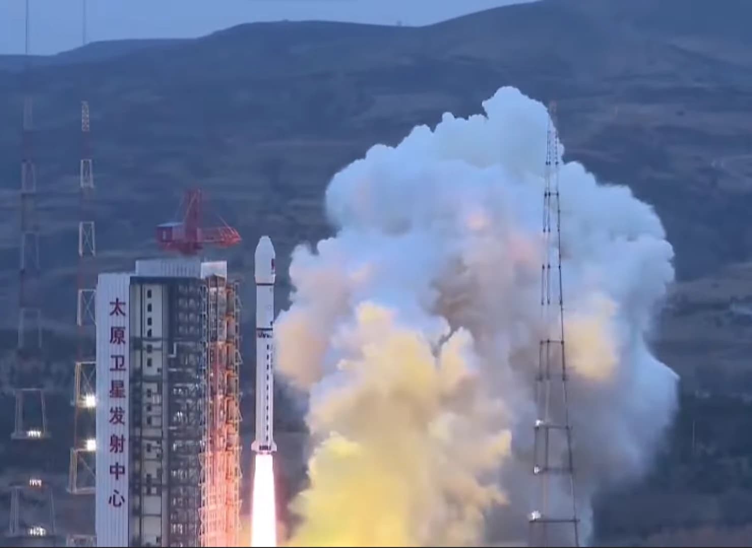 A rocket launching from a pad with large plumes of white and orange smoke.