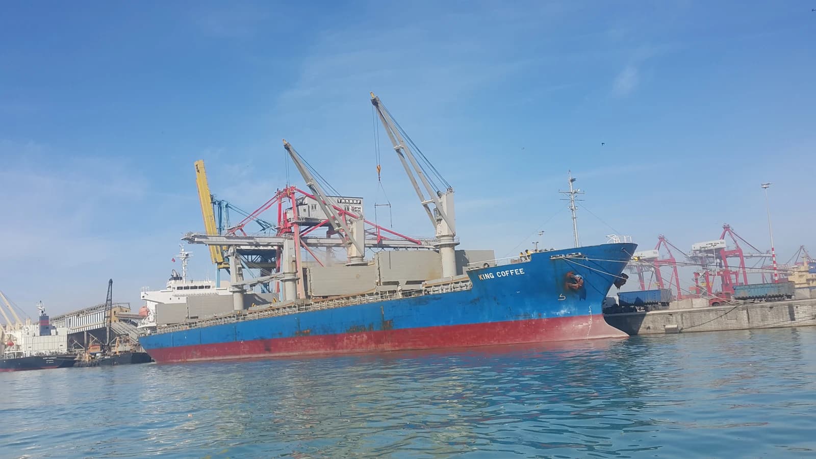 Cargo ship King Coffee docked at a port with cranes.