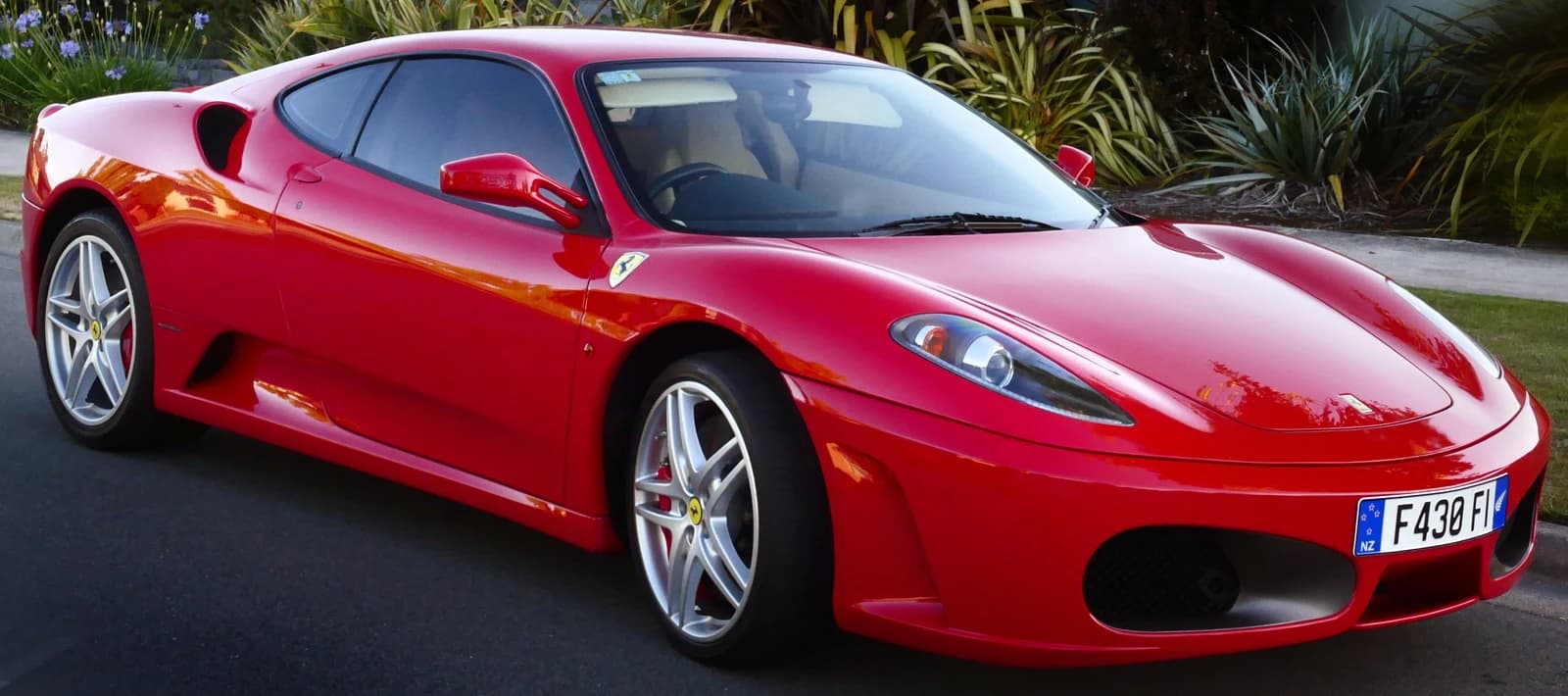 A gleaming red Ferrari F430 sports car parked outdoors on asphalt.