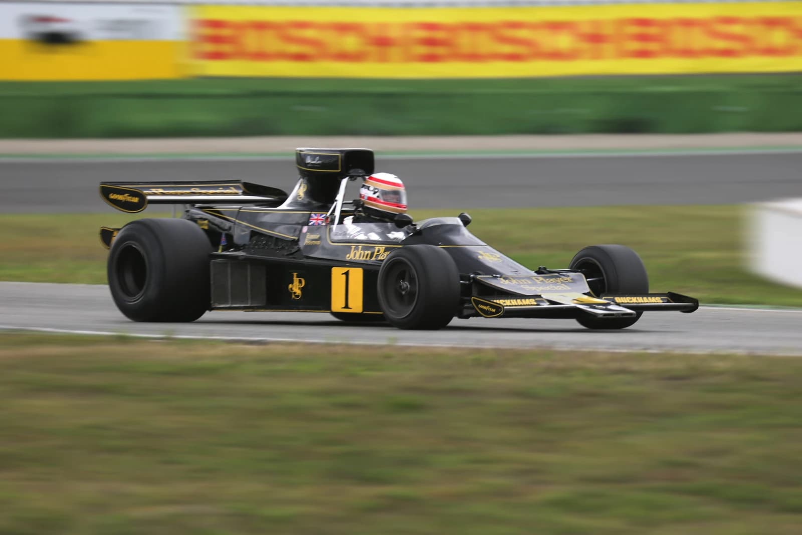 A black and gold Lotus 76 Formula 1 car with a driver on a race track.