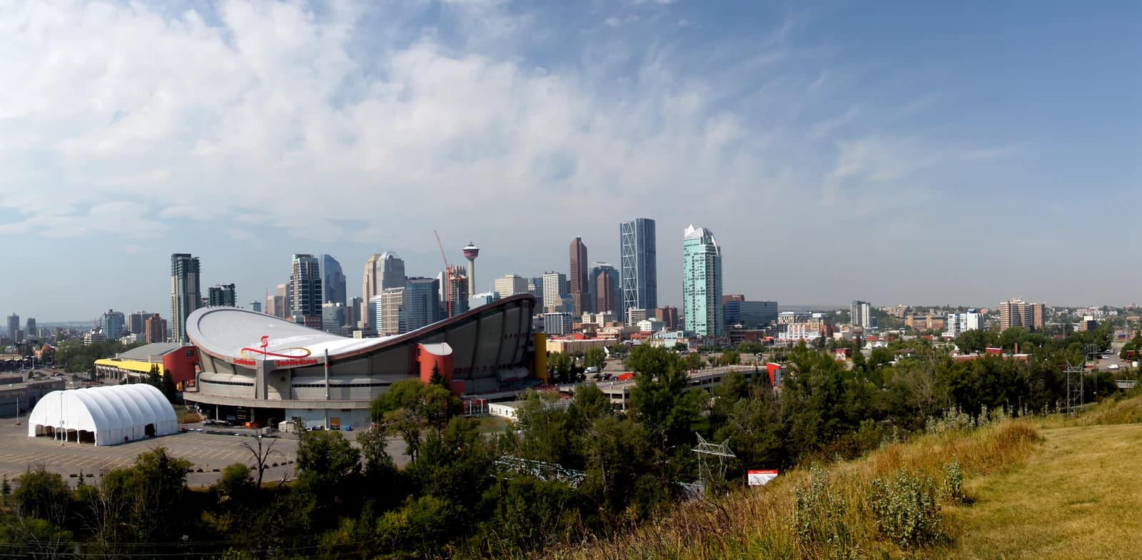 Calgary skyline with skyscrapers and Saddledome arena under a blue sky.