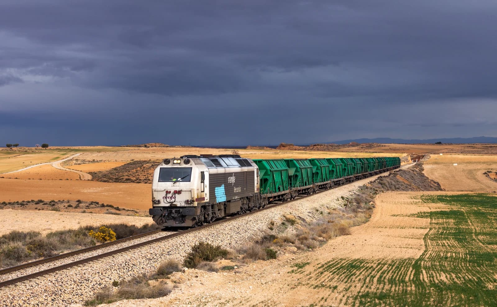Renfe Mercancías freight train 333.338 hauling green coal wagons across a rural landscape.
