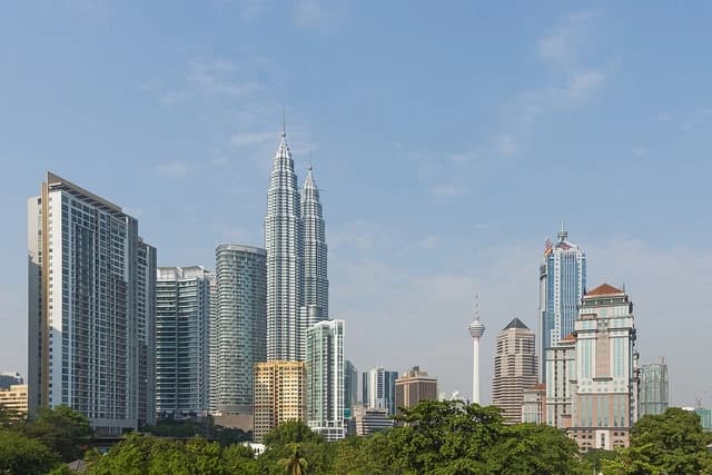Kuala Lumpur skyline with Petronas Towers and other buildings under a blue sky.