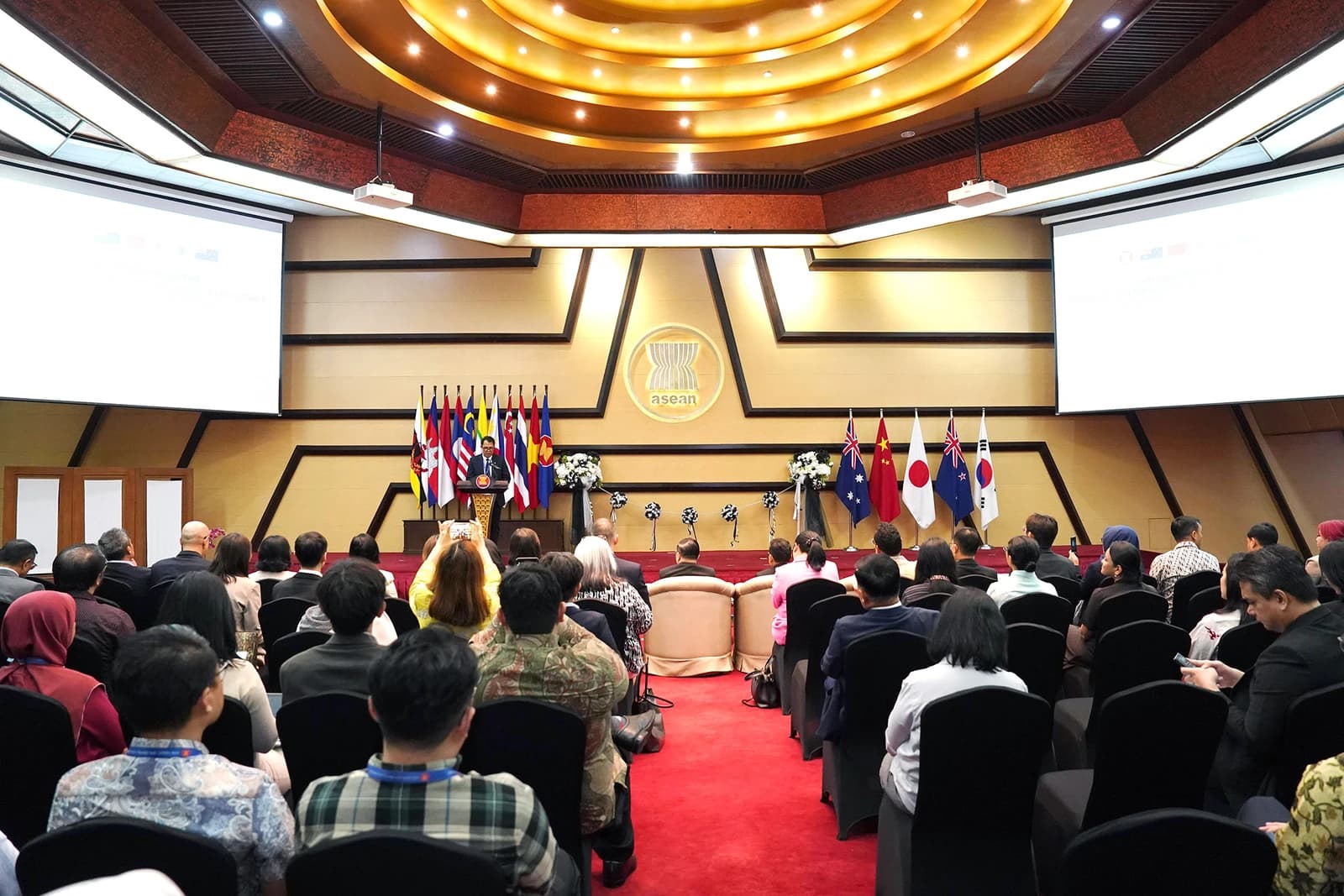 A speaker at a podium addressing an audience in the ASEAN Heritage Building Meeting room.