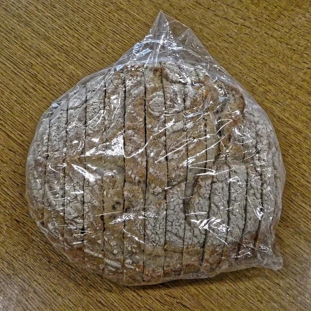 A pre-sliced sourdough loaf in clear plastic packaging resting on a wooden table.