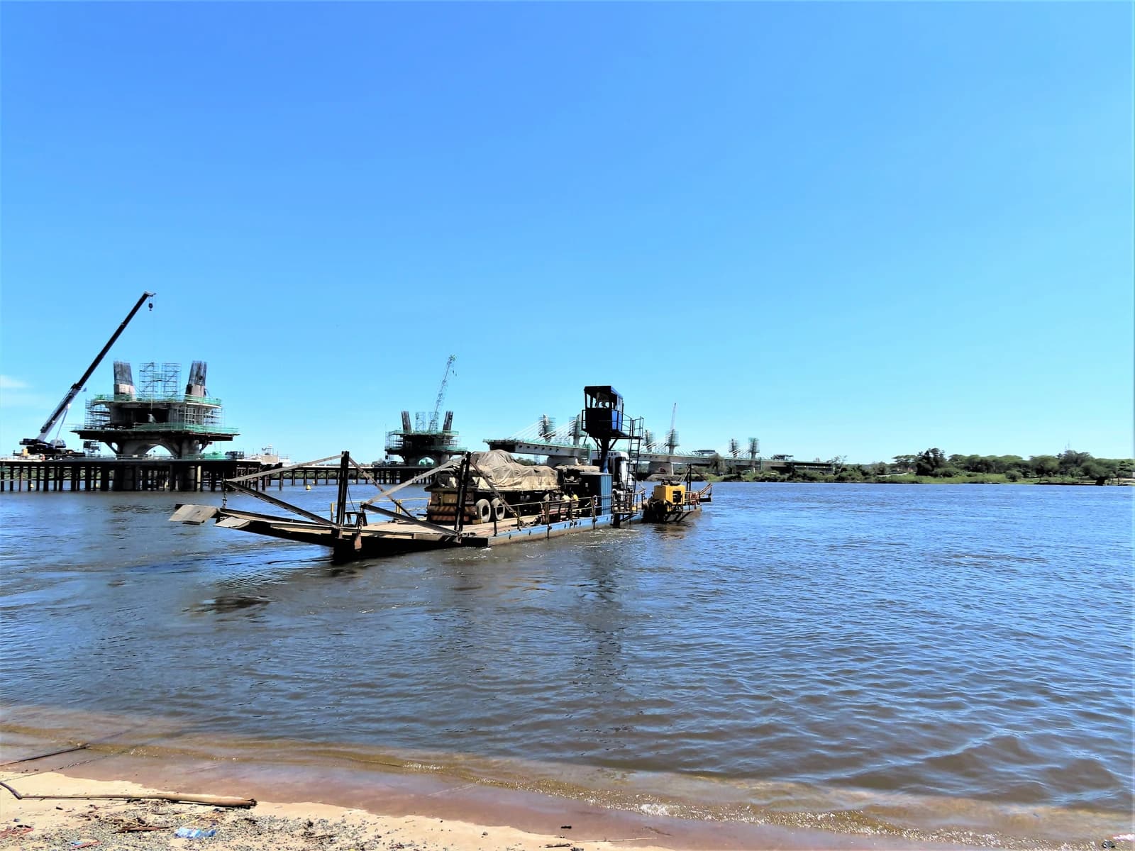Ferry boat carrying cargo on the Zambezi River next to a bridge construction site.
