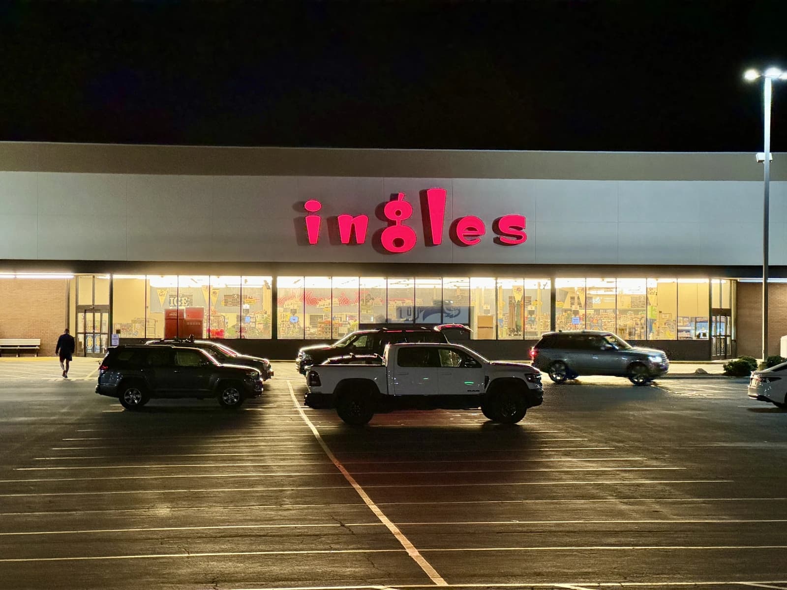 Ingles Supermarket exterior at night with its prominent red sign, cars parked in front.