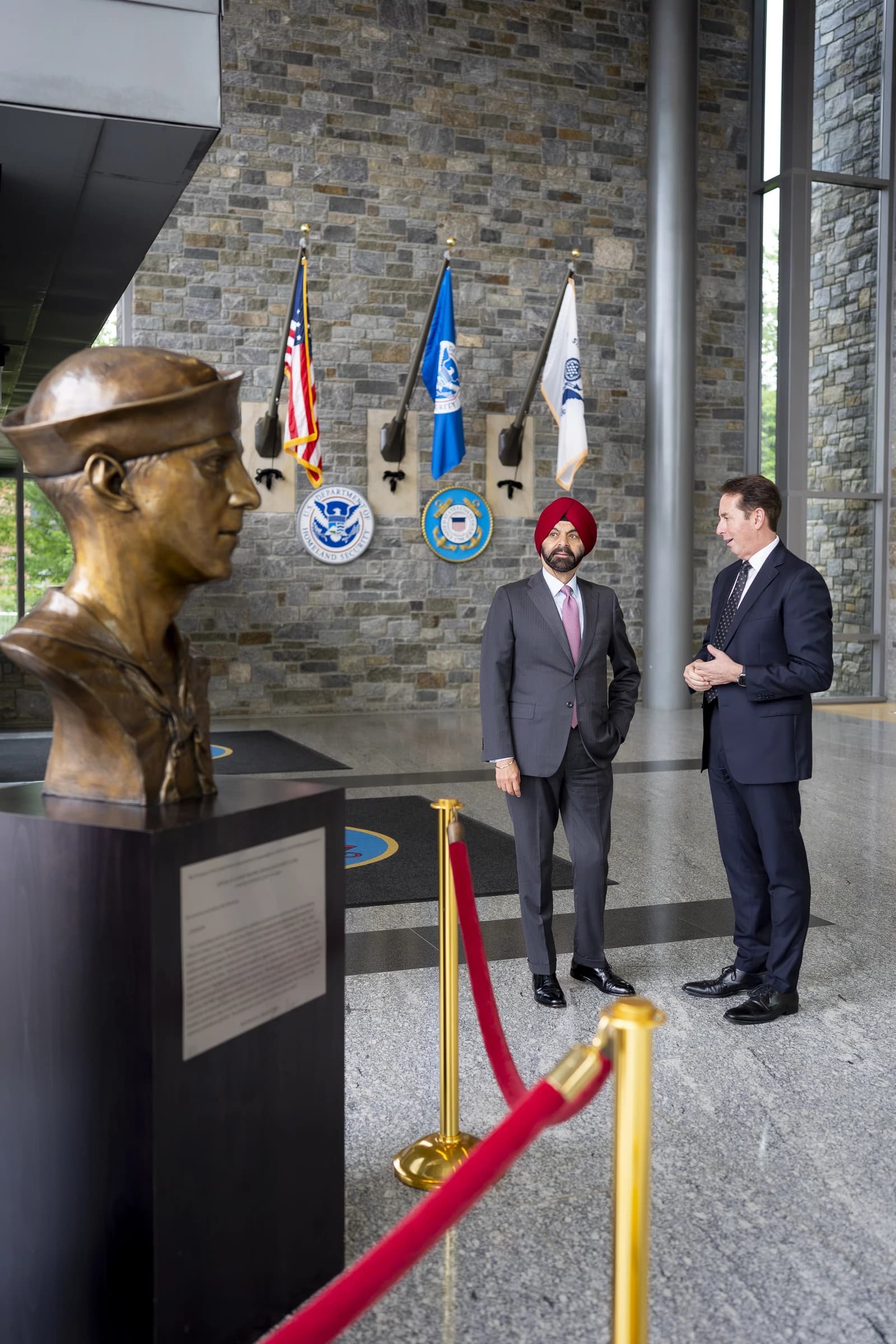 Ajay Banga, World Bank Group President, standing and conversing with a man in an indoor setting.