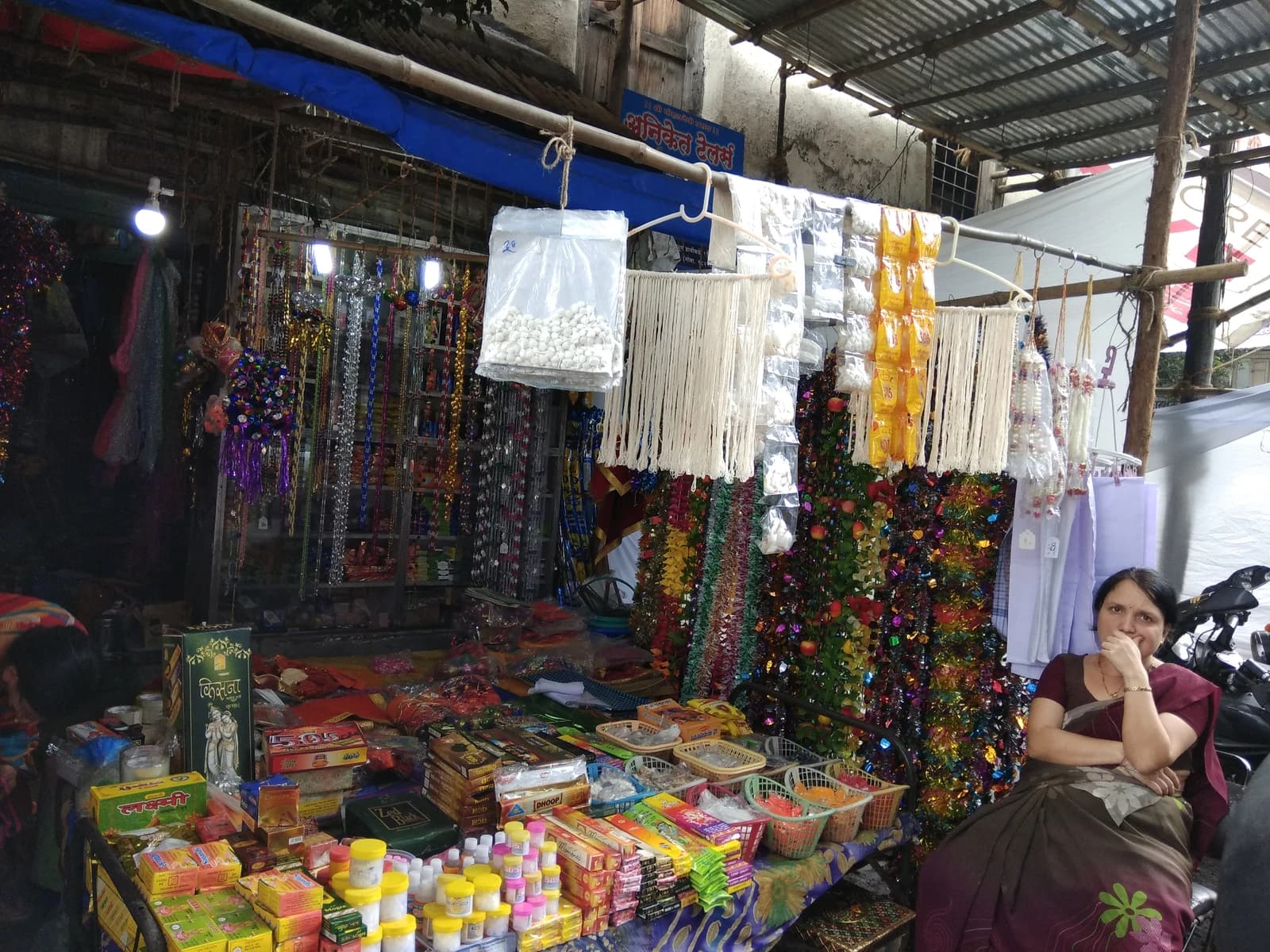 Woman seated by a stall laden with various items for religious festivals.