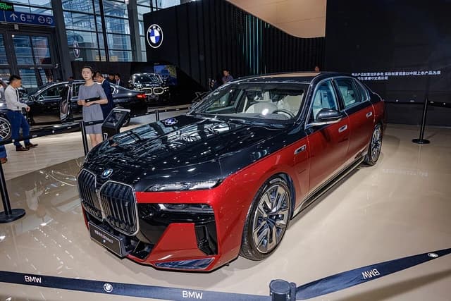 A two-tone red and black BMW i7 electric vehicle on display with a woman standing nearby.