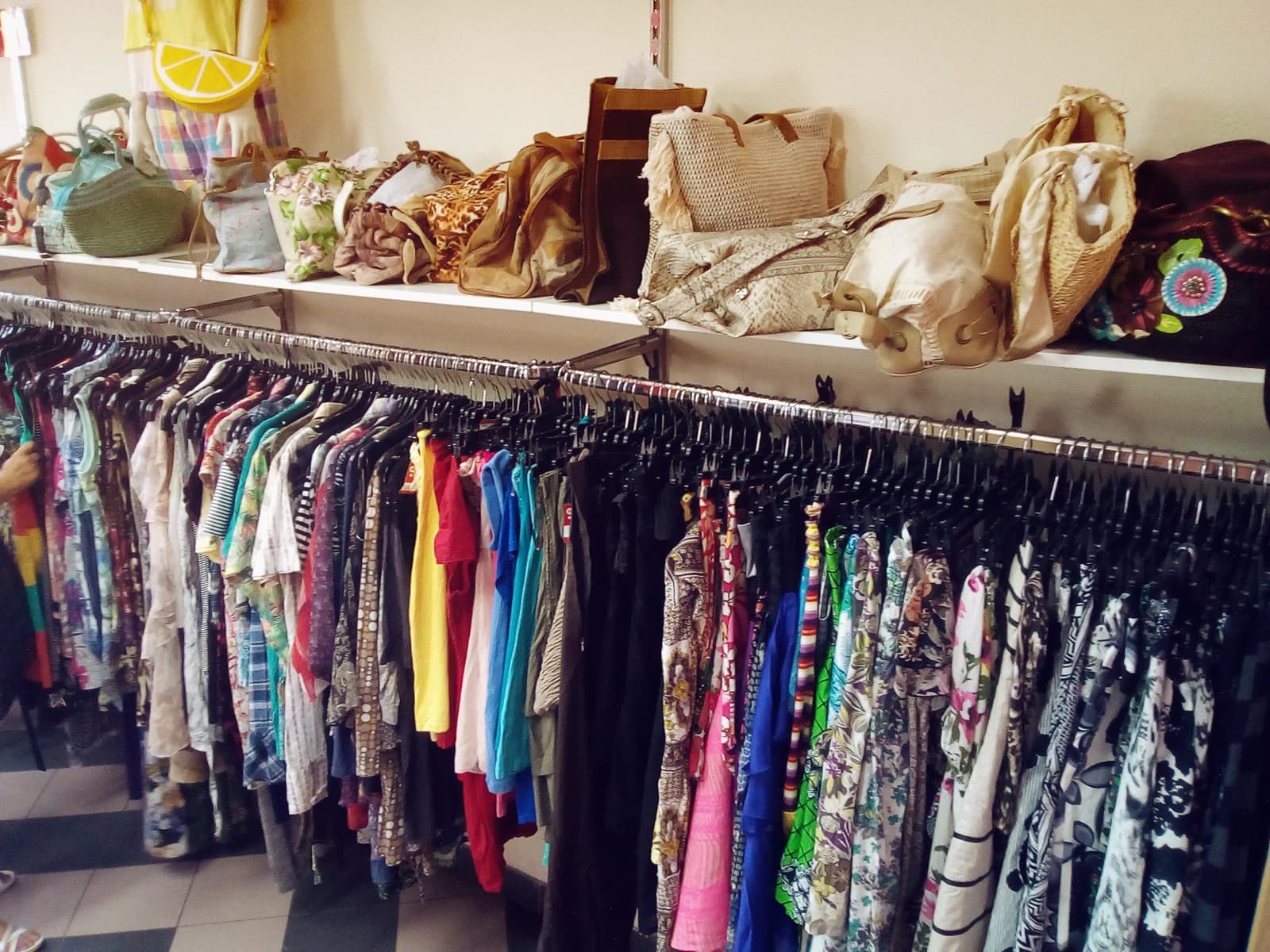 Racks of colorful clothing and shelves of assorted handbags in a second-hand store in Prague.