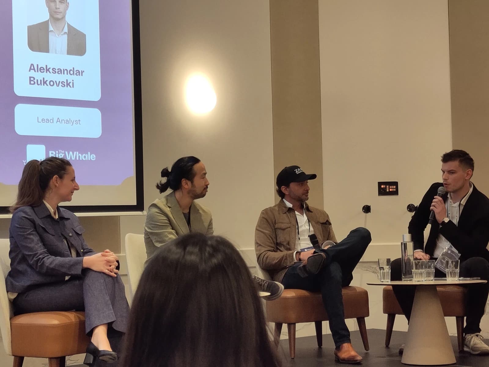 Four panelists sitting on stage at an industry conference, with one person speaking into a microphone.