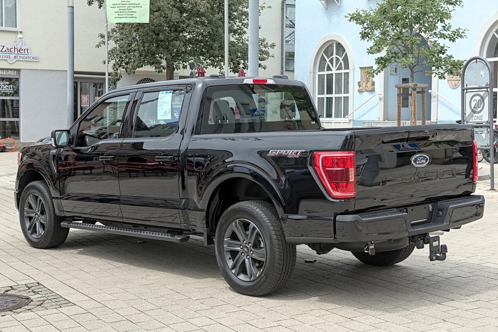 Black Ford F-150 pickup truck parked on a paved street in front of buildings.