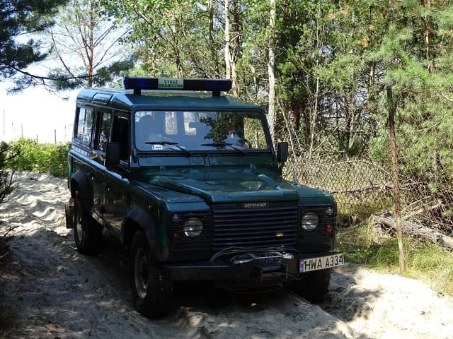 Polish Border Guard vehicle, a dark green Land Rover, on a sandy track.