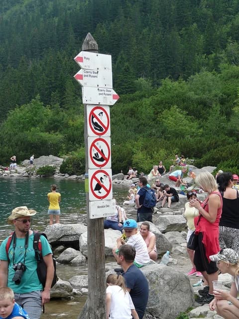 People gathered on rocks by a lake with a wooden signpost in Zakopane, Poland.