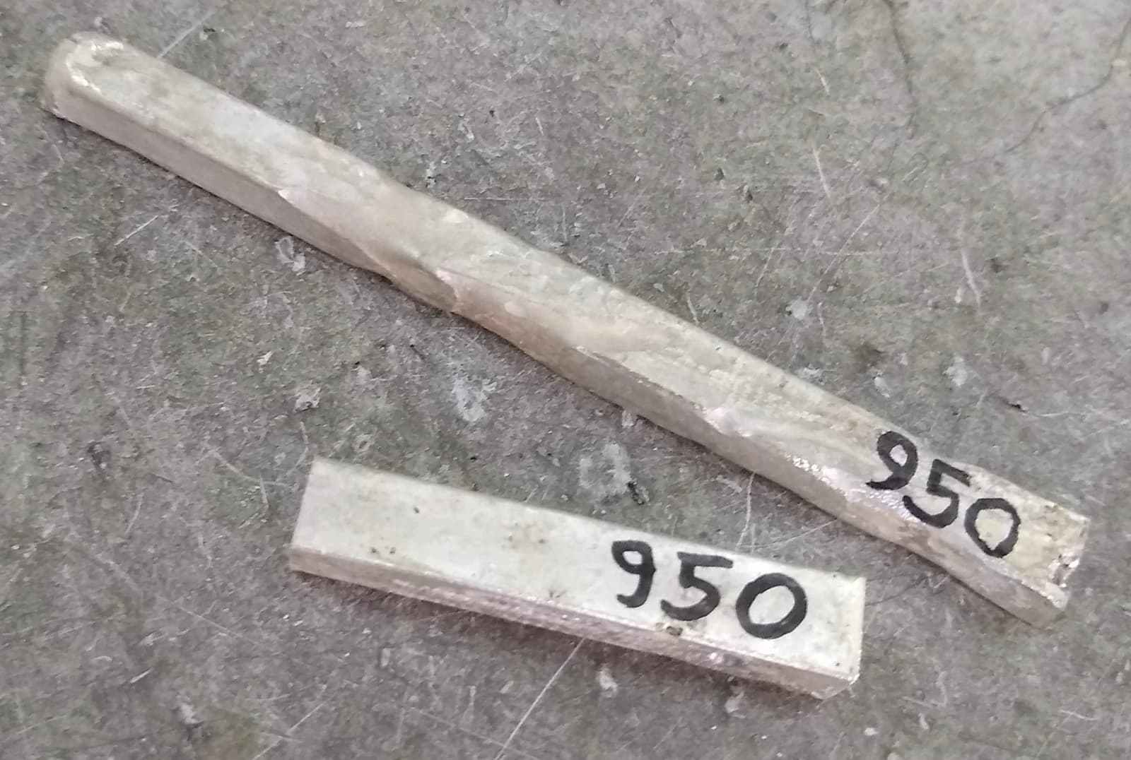 Two silver ingots, marked 950, resting on a textured gray surface.