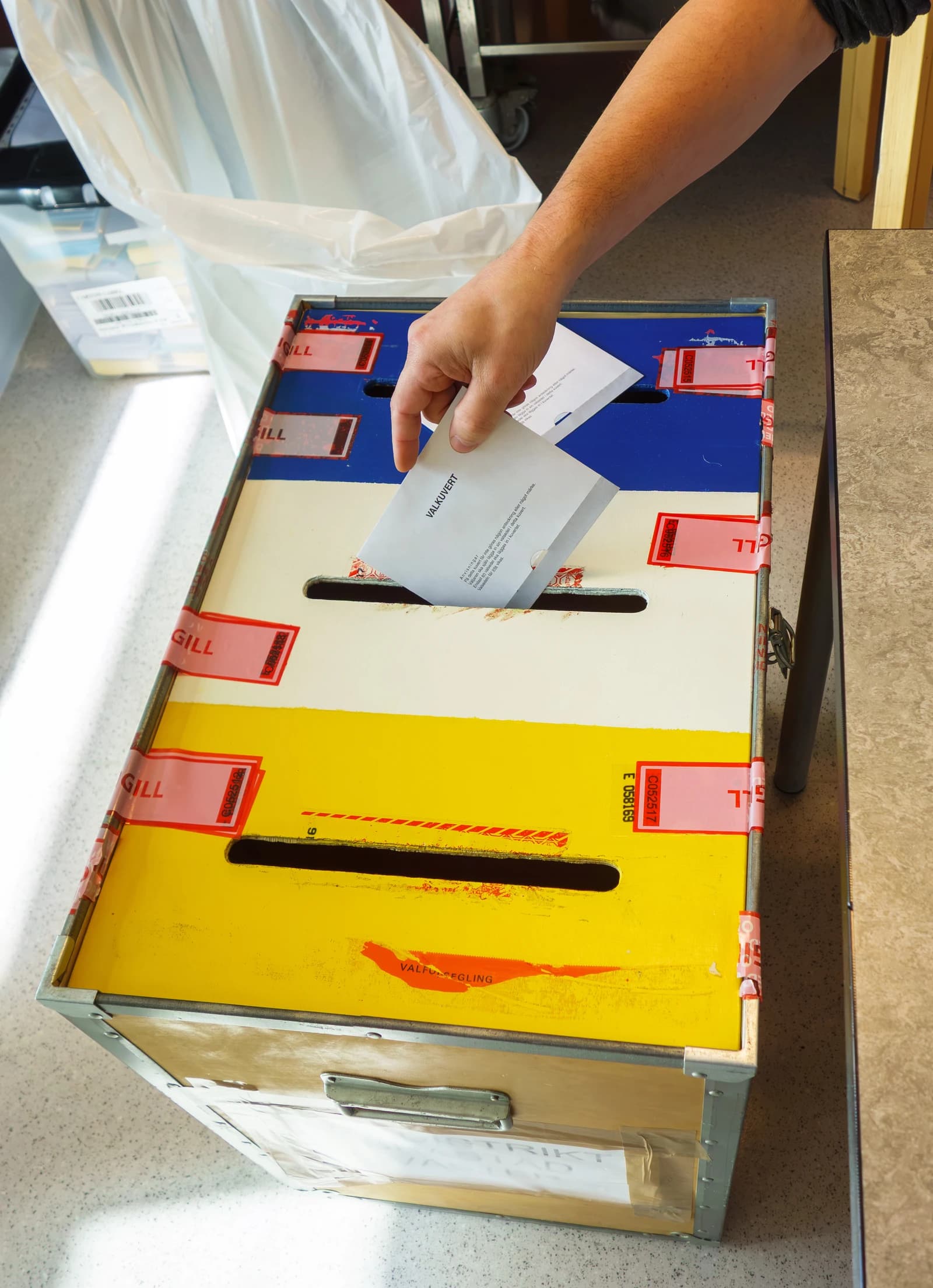 A person's hand placing a ballot envelope into a ballot box during an election.