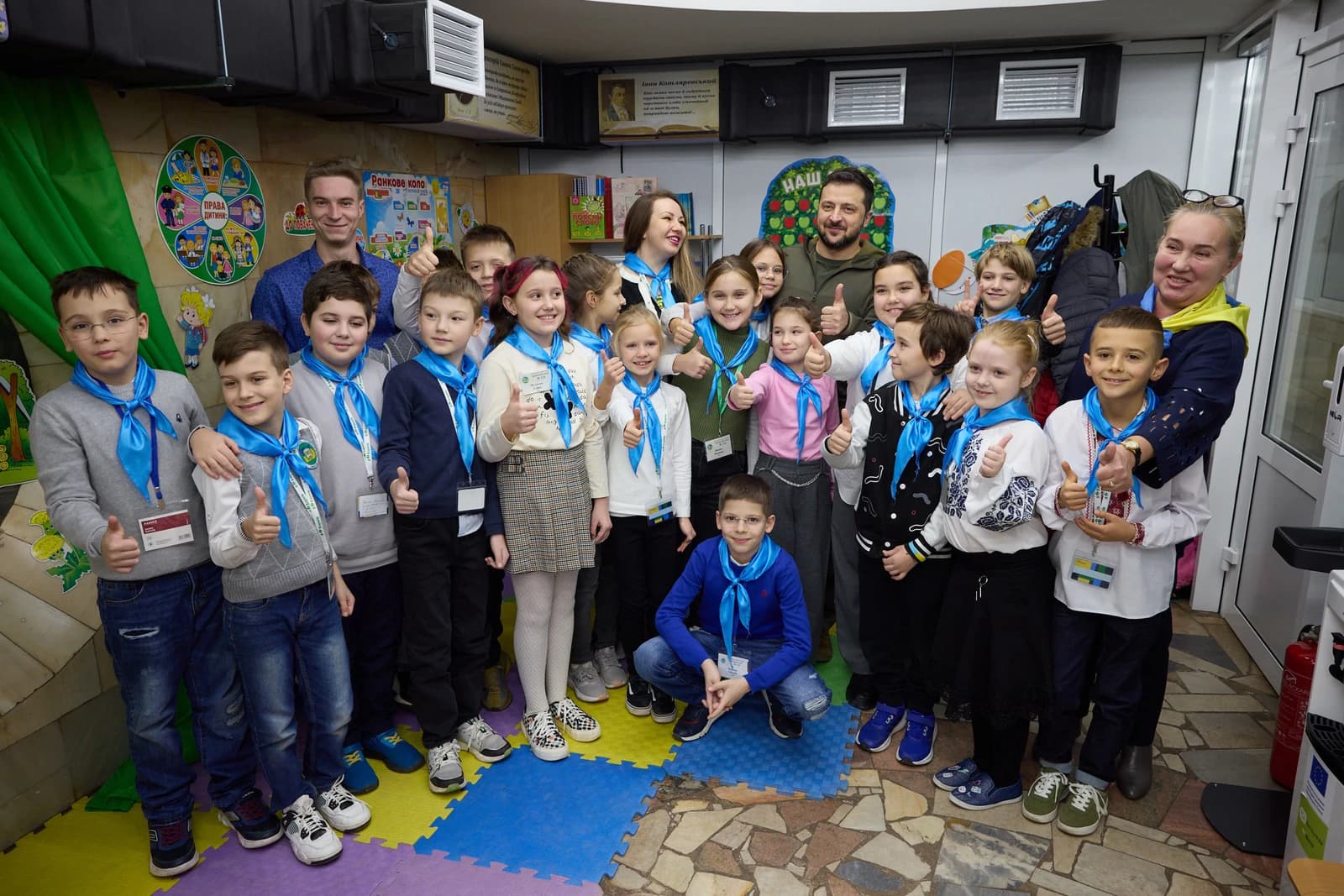Volodymyr Zelenskyy, President of Ukraine, poses with children giving thumbs up at a school.