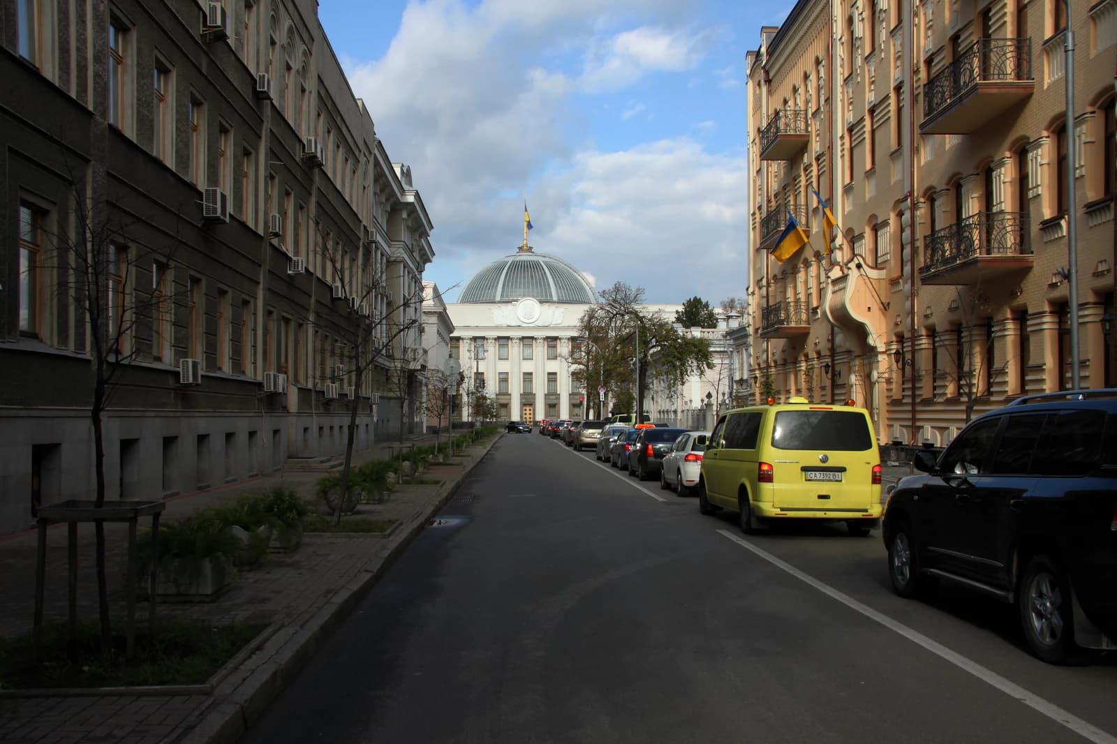 Parliament of Ukraine building, with a flag visible on its dome, seen from a street.