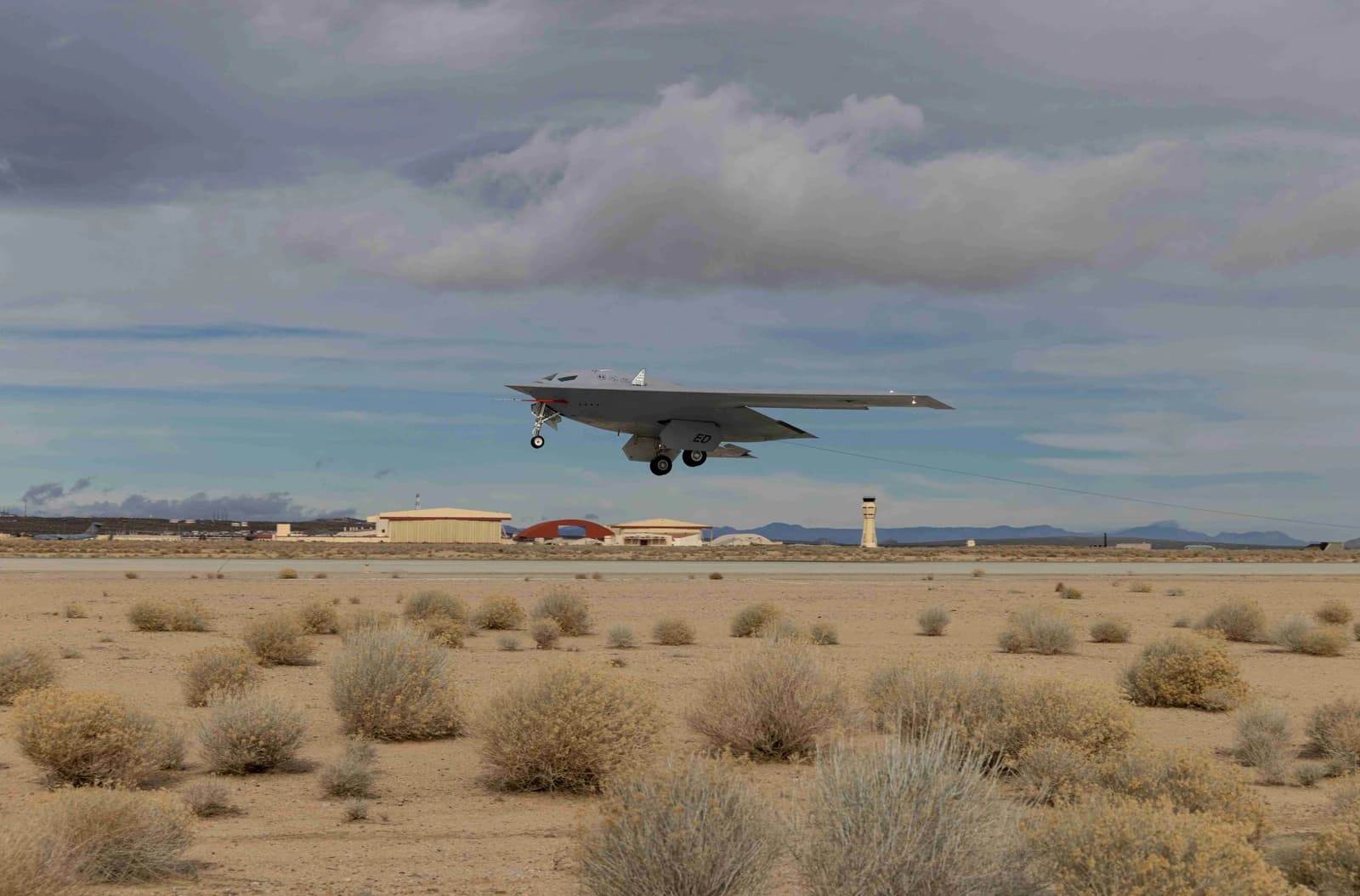 B-21 stealth bomber flying low over a runway at Edwards Air Force Base.