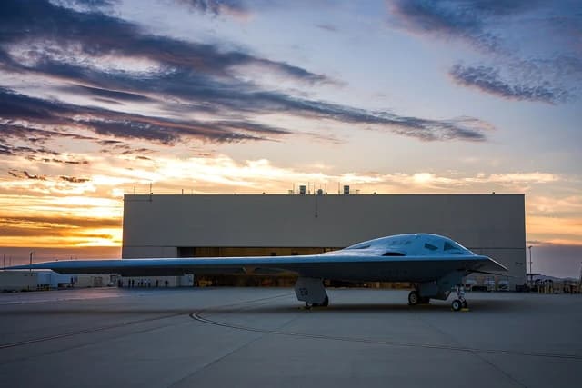 B-21 Raider stealth bomber parked on an airfield with a building in the background.