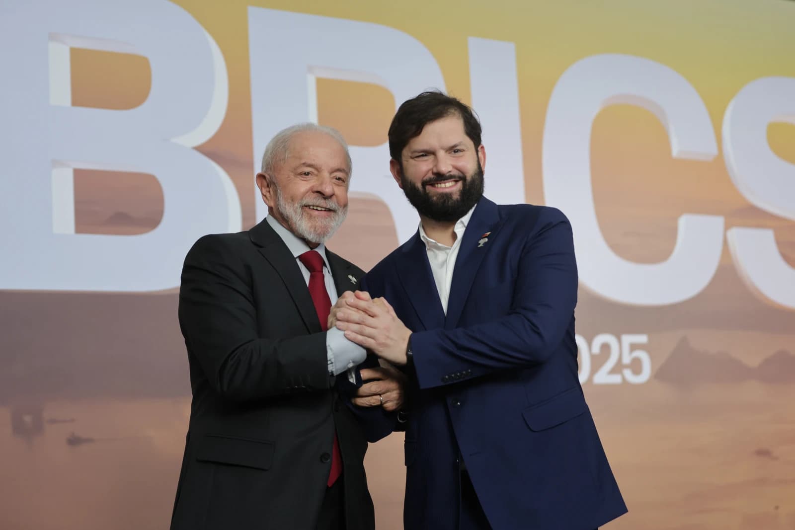 Luiz Inácio Lula da Silva and Gabriel Boric shake hands and smile at BRICS summit.