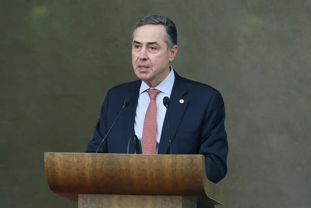 Brazilian Supreme Court Justice Roberto Barroso speaking into microphones at a wooden podium.