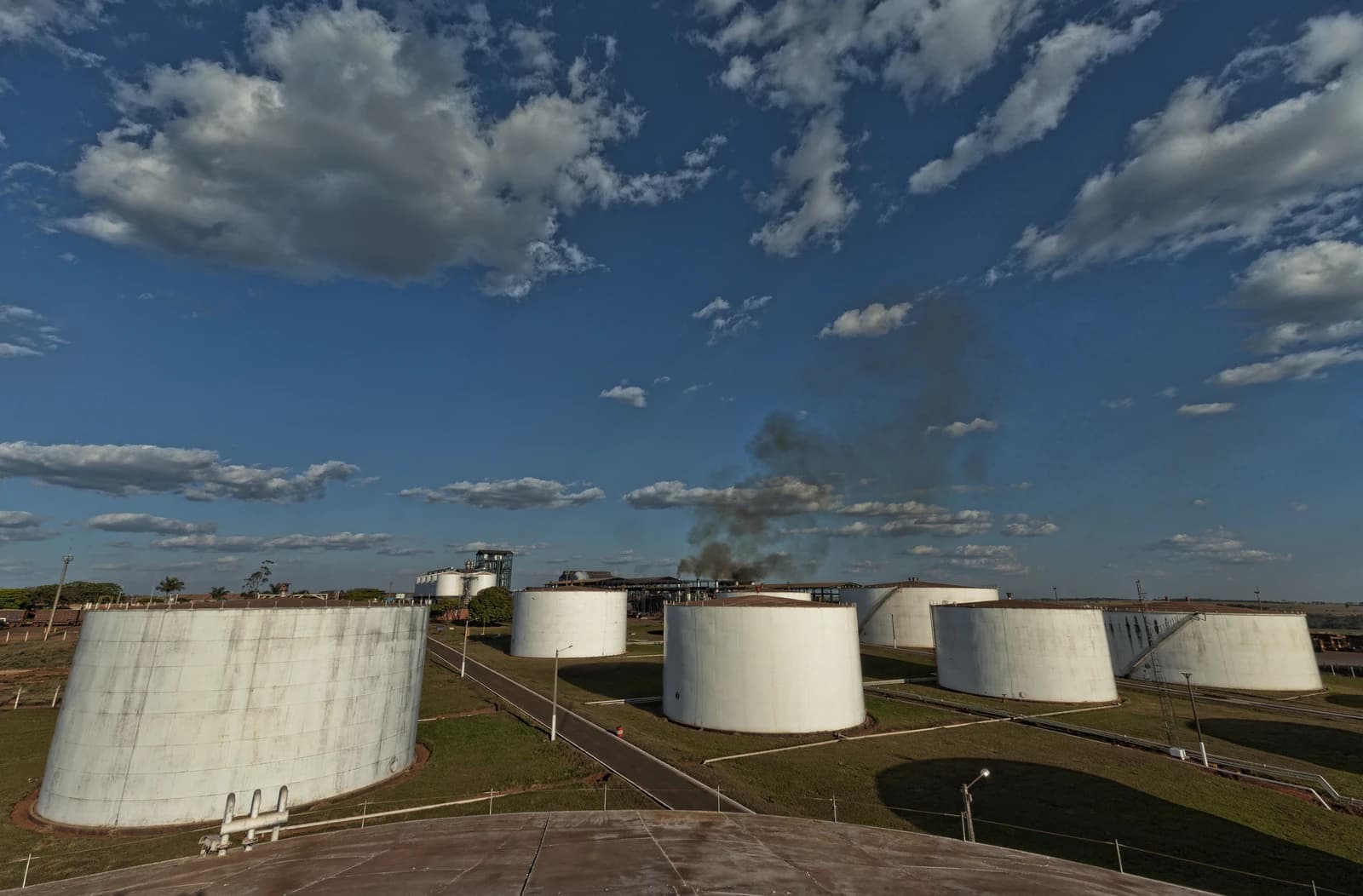 Large white storage tanks and industrial buildings under a blue sky with clouds.