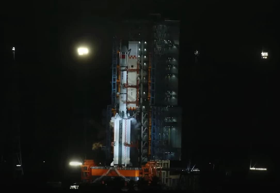 A Chinese Long March-7A rocket stands illuminated on a launchpad at night.