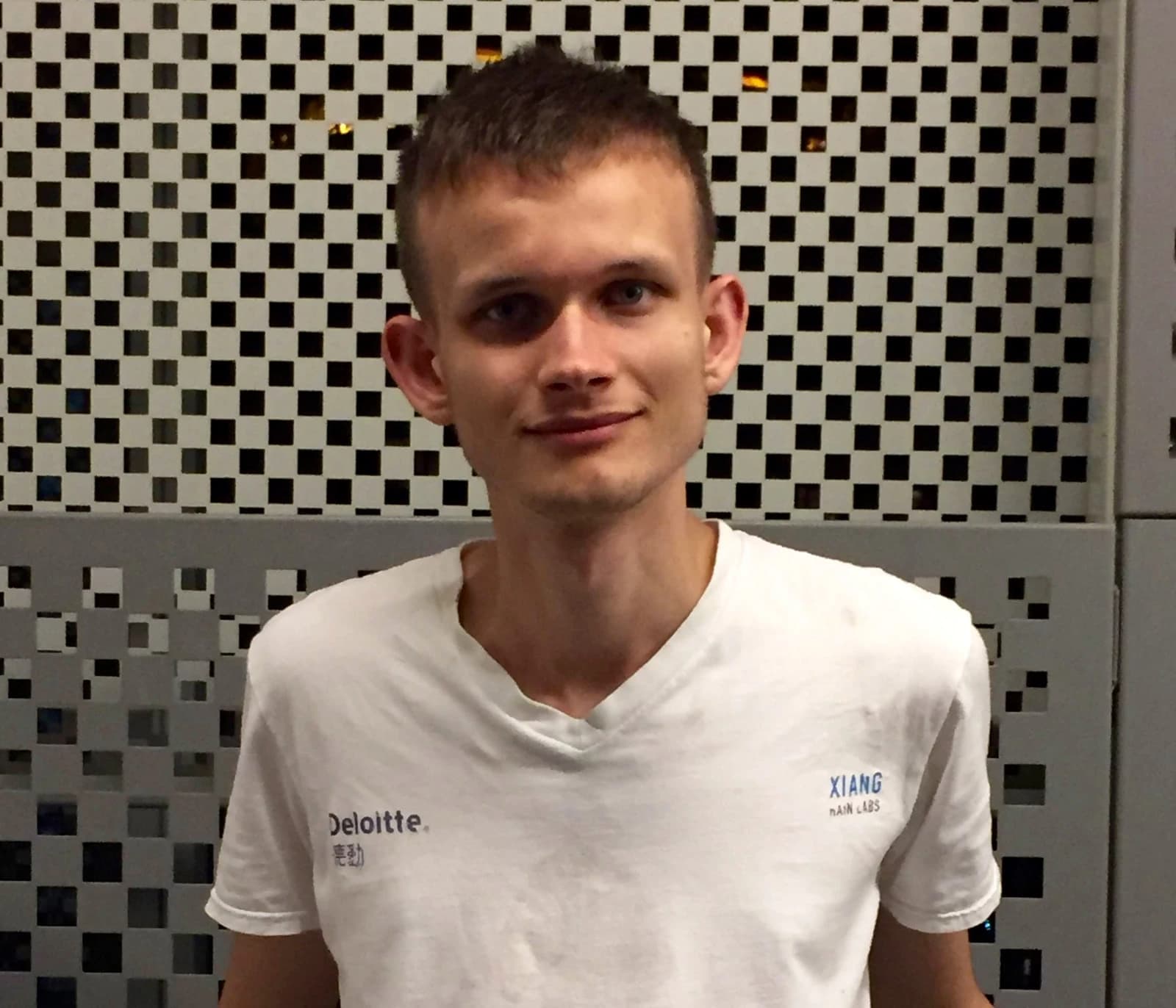 Vitalik Buterin, co-founder of Ethereum, stands in front of a patterned wall.